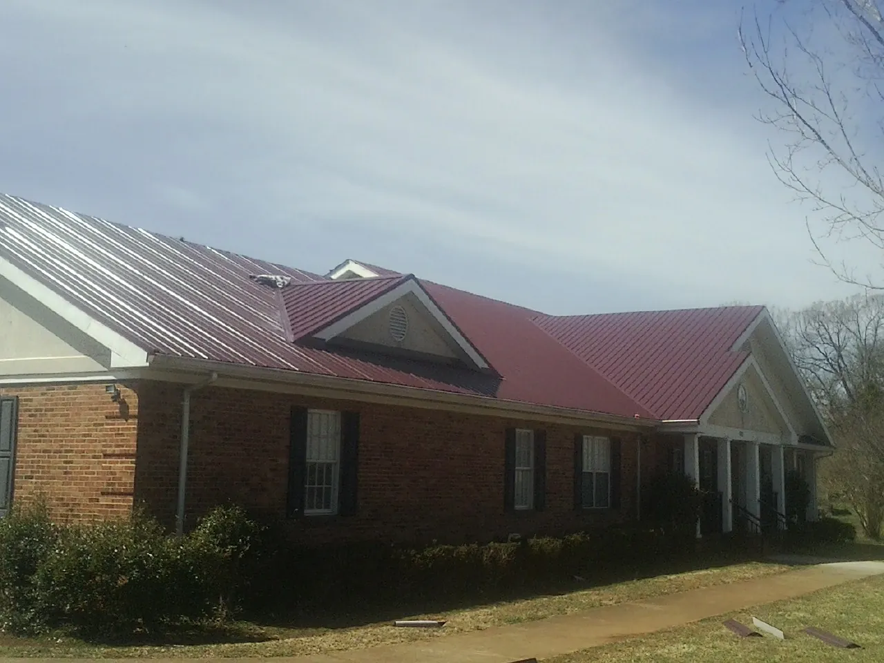 Red metal roof with gabled entries on a long brick building, from a Hail Damage Roof Repair job in Farmington
